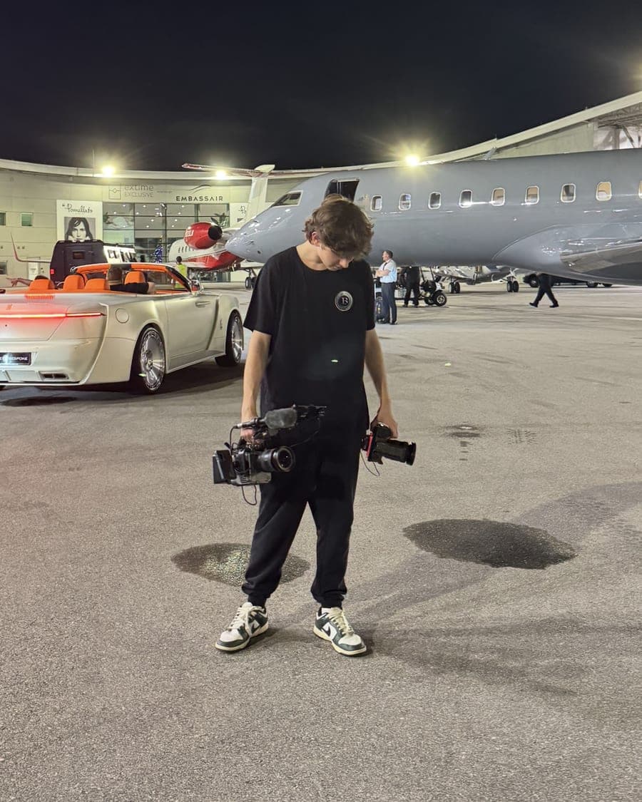 Carson filming on the tarmac beside a private jet and custom convertible at night
